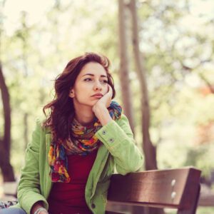 Unhappy girl sitting at bench Thoughtful woman in the park